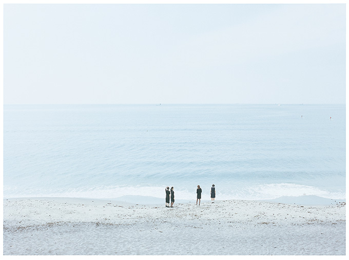 海辺を歩く四姉妹を遠くからみつめる写真